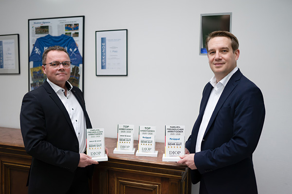 Auszeichnungen Top Arbeitgeber Zwei Mitarbeiter in Anzügen präsentieren lächelnd die Auszeichnungen für Knüppel und Excor.